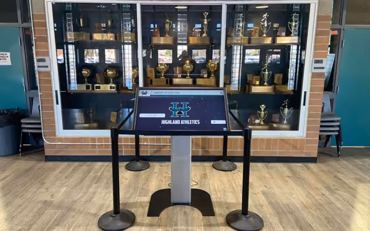 A freestanding touchscreen kiosk in front of a trophy case