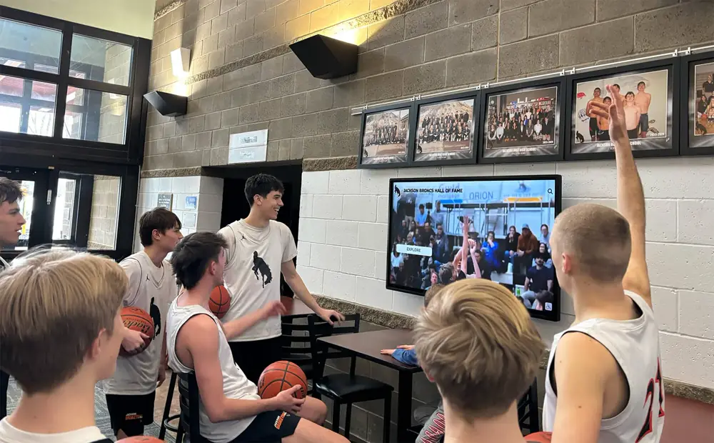 Basketball players gather around a wall-mounted display of team photos