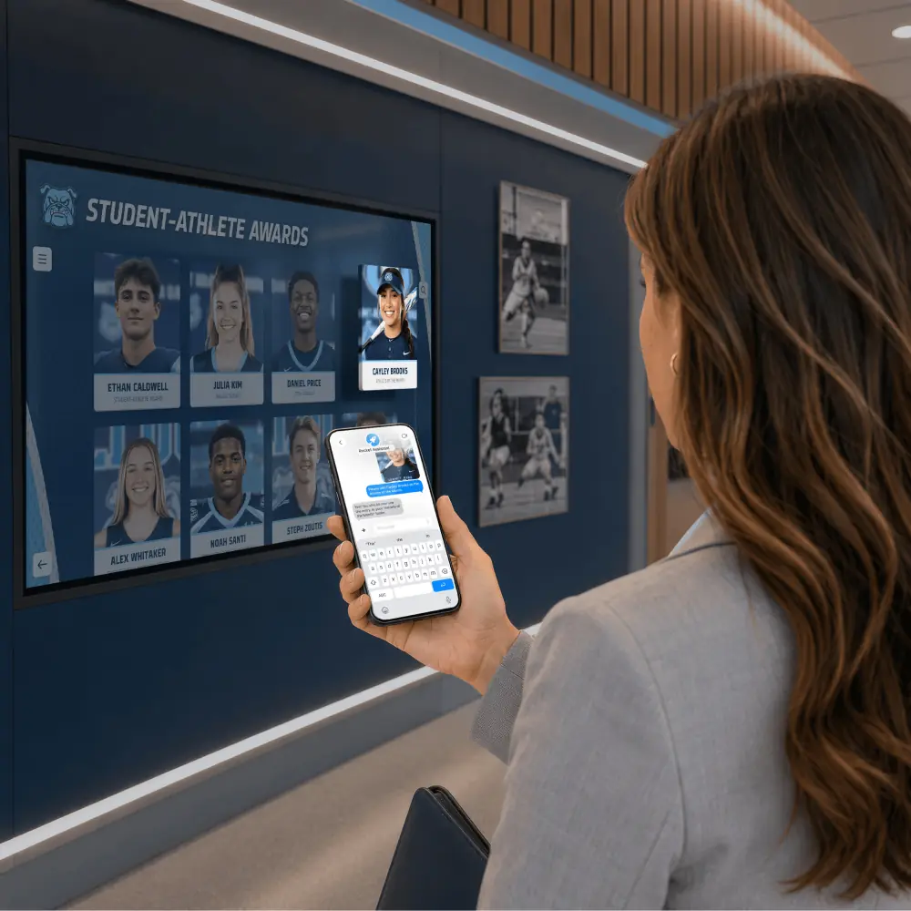 A staff member holds a phone in front of a Student-Athlete Awards display