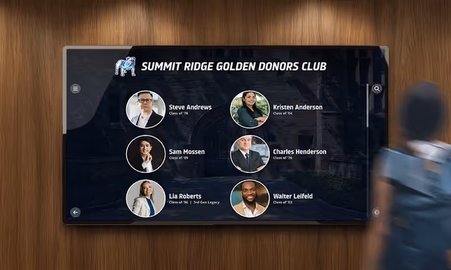 A donor club touchscreen with alumni portraits on a wood-paneled wall